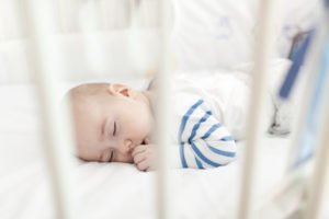 A small child takes a nap in a white blanketed crib